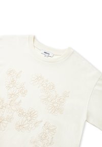 Crème-kleurig T-shirt met korte mouwen, voorzien van een lichtbeige bloemenborduurpatroon op de voorkant, ronde halslijn en een zachte textuur.