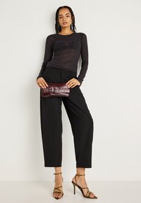 Top negro de manga larga y transparente con pequeños puntos blancos, combinado con pantalones negros de cintura alta y sandalias de tacón alto en color oliva. Bolso de mano burdeos.