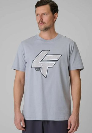 Man draagt lichtgrijs T-shirt met groot gestileerd "4F"-logo en "SPORTS WEAR" tekst, staand tegen een effen grijze achtergrond.