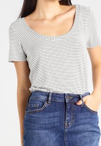 Bluzka z okrągłym dekoltem i krótkim rękawem w białym kolorze z czarnymi poziomymi paskami, w połączeniu z niebieskimi dżinsami z wysokim stanem, zapinanymi na guzik.