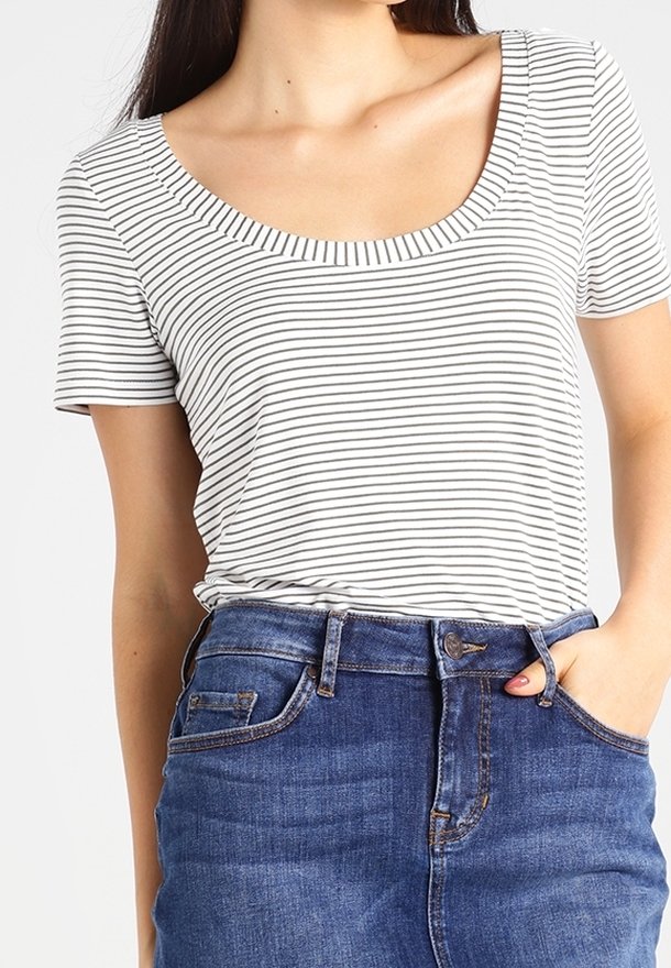 Bluzka z okrągłym dekoltem i krótkim rękawem w białym kolorze z czarnymi poziomymi paskami, w połączeniu z niebieskimi dżinsami z wysokim stanem, zapinanymi na guzik.