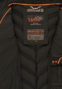 Black insulated jacket interior with quilted texture, orange accents, a tag displaying brand and care information, and an inner pocket.