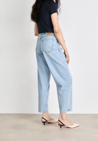 Jasnoniebieskie, wysokie dżinsy o luźnym kroju, z tylnymi kieszeniami i przeszyciami. Zestawione z czarną, dopasowaną koszulą i beżowymi klapkami.