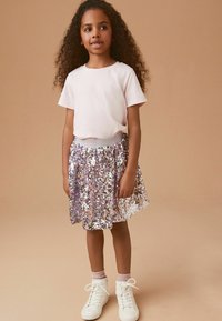 T-shirt rosa a maniche corte abbinato a una gonna scintillante di paillettes nelle tonalità di rosa e argento, completato da sneakers bianche alte.