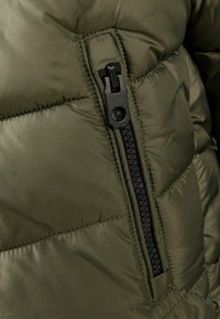 Doudoune vert olive avec une fermeture éclair noire à l'avant, dotée de sections matelassées et d'une texture de tissu lisse et brillante.