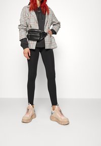 Rutig kavaj, grå hoodie, svarta leggings och chunky beiga och rosa sneakers. Midjeväska i svart. Släta ytor och olika mönster.