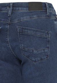 Blugi din denim albastru închis, vedere din spate, cu bucle pentru curea, un buzunar cusut în spate și o etichetă de brand din piele neagră la talie.