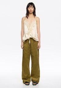 Camisón de satén crema con detalle de encaje y lazo en el frente, combinado con pantalones de pierna ancha de talle alto en verde oliva con tejido texturizado y bolsillos.
