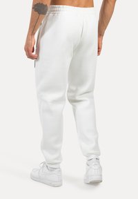 Pantalones de chándal blancos hechos de una tela suave, con cintura elástica y bolsillos laterales, combinados con zapatillas blancas.