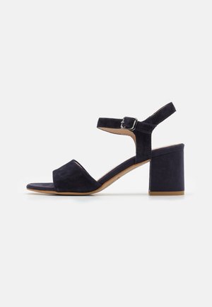 Sandalo in suede blu navy con una larga fascia per le dita, una stretta fascia alla caviglia fissata da una fibbia in argento e un tacco a blocco. Suola in gomma piatta.