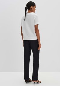 White textured short-sleeve top paired with black fitted pants and black heeled sandals. The top features a collar and a loose fit.