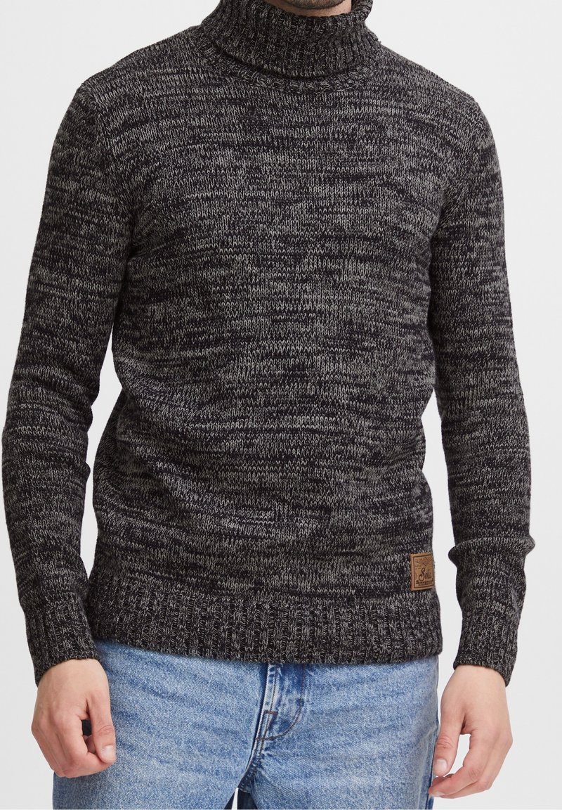 Maglione a collo alto lavorato a maglia di un grigio scuro con sfumature più chiare, caratterizzato da un colletto e polsini a coste, e un'etichetta del marchio tessuta sull'orlo.