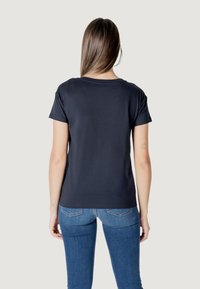 T-shirt blu scuro con maniche corte, collo rotondo e una texture liscia. Sul retro presenta una sottile cucitura decorativa. Indossato con jeans blu.