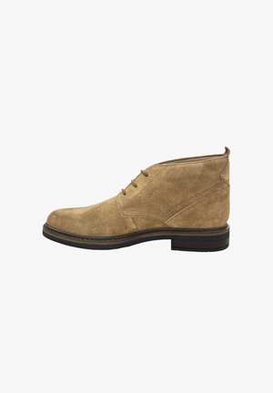 Bottine en suède tan avec un bout arrondi, un laçage à l'avant et une semelle en caoutchouc marron foncé contrastante. Comprend des détails de couture subtils.