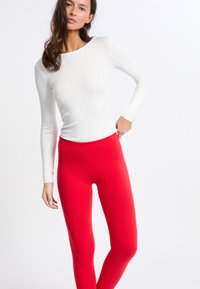 Blusa blanca de manga larga y canalé combinada con leggins rojos vibrantes. La blusa presenta un escote barco; los leggins tienen un diseño liso y ajustado.