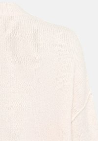 Gros plan sur un tissu tricoté beige clair montrant la texture et le détail du col côtelé d'un vêtement.