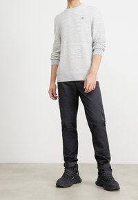 Pull en tricot gris avec un col rond, associé à un pantalon slim noir et des bottes de randonnée noires texturées avec lacets et soutien de la cheville.