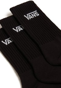 Svarta strumpor i ribbat tyg, med en vit "VANS"-logotyp på mudden. Tre par staplade prydligt, som visar en enhetlig design och textur.