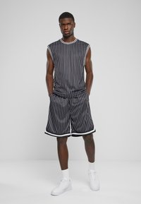 Costum sport fără mâneci, cu dungi negre și albe, cu pantaloni scurți cu talie elastică, având borduri contrastante și asortat cu adidași albi.