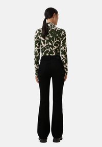Bodies s dlouhým rukávem v zeleno-krémovém abstraktním vzoru, spárované s černými vysokými zvonovými džíny. Zadní pohled ukazuje zip a knoflík.
