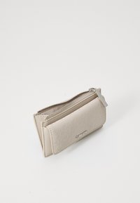 Beige falsk lær lommebok med et strukturert mønster, glidelås lukking, og en sølvfarget logo aksent på forsiden. Kotrakt og rektangulær form.