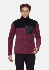 Bordowa kurtka z polaru z czarną górną częścią, wysokim kołnierzem i kieszenią na piersi zamykaną na zamek. Posiada kieszenie boczne na zamek oraz gładką fakturę.