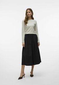 Gestreepte langsliggende top in crème en zwart, gecombineerd met een zwarte, geplooide midi-rok. Bruine sleehakken met decoratieve accenten maken de outfit af.