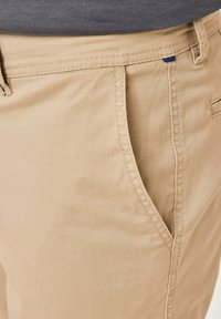 Khaki trousers featuring a textured fabric, straight leg design, and side pocket with subtle blue accent near the waistband.