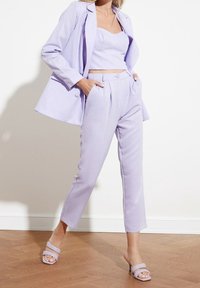 Lila tweedelig pak met een getailleerde crop top en op maat gemaakte broeken met een hoge taille. Gladde, lichte stof met minimale details.