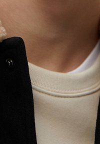 Sort faux suede jakke med beige krave, lagdelt over en cremefarvet sweatshirt med ribbede manchetter og rund halsudskæring.