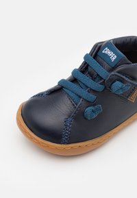 Chaussure en cuir marine avec des lacets bleus, bout rond, accents cousus et semelle en caoutchouc marron. Étiquette logo cousue sur la languette.