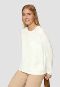 Witte pullovertrui met een geribde halslijn en verlaagde schouders, gecombineerd met beige broek. Soepele textuur en relaxte pasvorm.