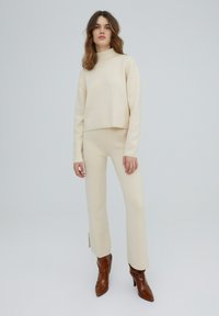 Crème-kleurige bijpassende set met een kort, langemouwen top en slim-fit broek, gecombineerd met bruine, hoge, gestructureerde enkellaarsjes.