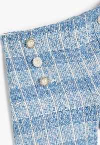 Tela de tweed azul y blanco con un patrón texturizado; cuenta con tres botones decorativos de perlas en el lateral, realzando el diseño.