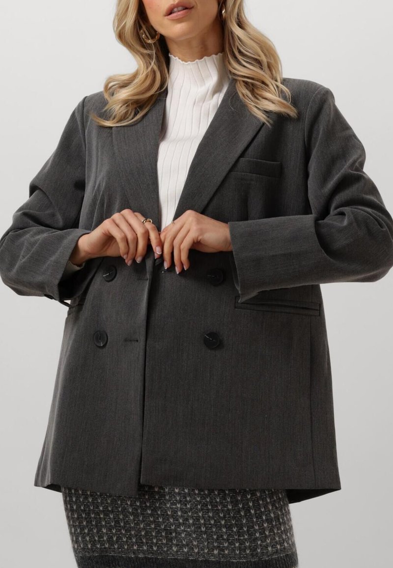 Harmaa kaksirivinen bleiseri, jossa on teksturoitu kangas, suuret mustat napit ja yksi rintatasku. Yhdistetty valkoisen ribatun paidan kanssa.