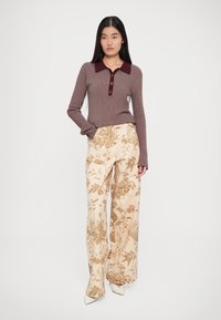 Bluză lungă cu mâneci, de culoare maro cu dungi, având guler și nasturi căpșuni, asortată cu pantaloni largi din crem, cu un model floral.