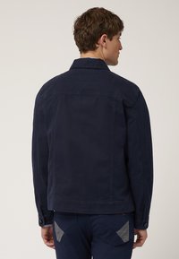 Navyblauwe jas met een rechte snit, voorzien van een klassieke kraag, knoopsluiten en een gladde textuur. De achterkant toont een eenvoudig ontwerp.