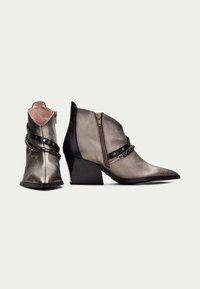 Botas de cuero metálico hasta el tobillo con puntera afilada, tacón grueso, cremalleras laterales y detalles en cuero negro alrededor de la parte media del pie. Incluye detalle de cadena.