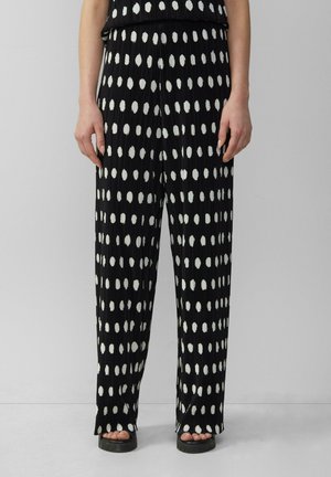 Pantalons en tissu noir texturé avec des pois blancs irréguliers. Coupe ample avec une taille haute et des jambes larges, adaptés pour une tenue décontractée.