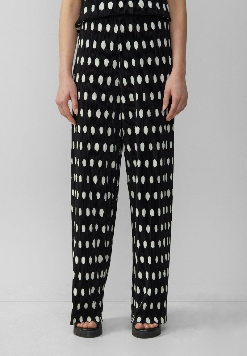 Pantalons en tissu noir texturé avec des pois blancs irréguliers. Coupe ample avec une taille haute et des jambes larges, adaptés pour une tenue décontractée.
