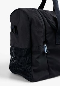 Bolso de deporte de tela negra con un exterior liso, cierre de cremallera, bolsillo lateral de malla y asas resistentes para llevar.