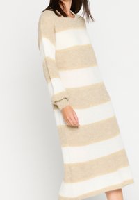 Beige och vit randig stickad klänning med långa ärmar och en avslappnad passform. Mjuk textur, knälång, med rund halsringning och manschetter på ärmarna.