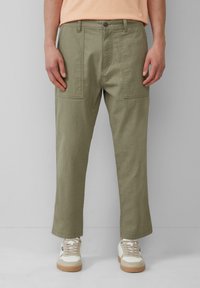 Khaki cargobroeken met een rechte snit, voorzien van grote zijzakken en een soepele textuur. Gecombineerd met witte sneakers.