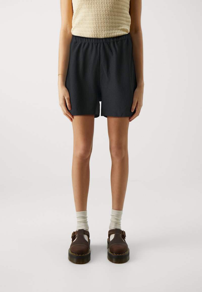 Black shorts with an elastic waistband, textured fabric, and side pockets, paired with brown shoes and light gray socks.