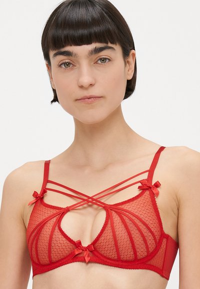 Sarkana caurspīdīga tīkliņa krūšturis ar sarežģītiem izgriezumiem un krustenisku siksnu dizainu. Uz siksnām ir nelielas satīna loki, teksturēta auduma un mīkstas malas.