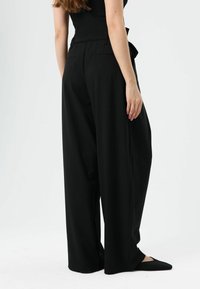Pantalon noir à jambes larges en tissu lisse, doté d'une taille haute, de poches latérales et de détails subtils sur les poches arrière.
