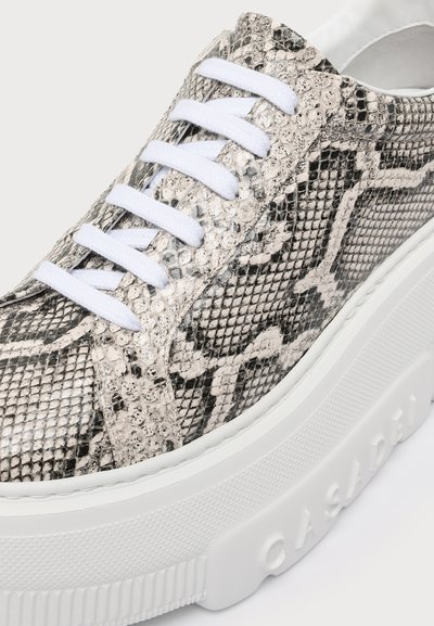 Baskets avec lacets blancs et semelle blanche épaisse, présentant un motif peau de serpent noir et gris et le nom de la marque en relief sur le côté de la semelle.