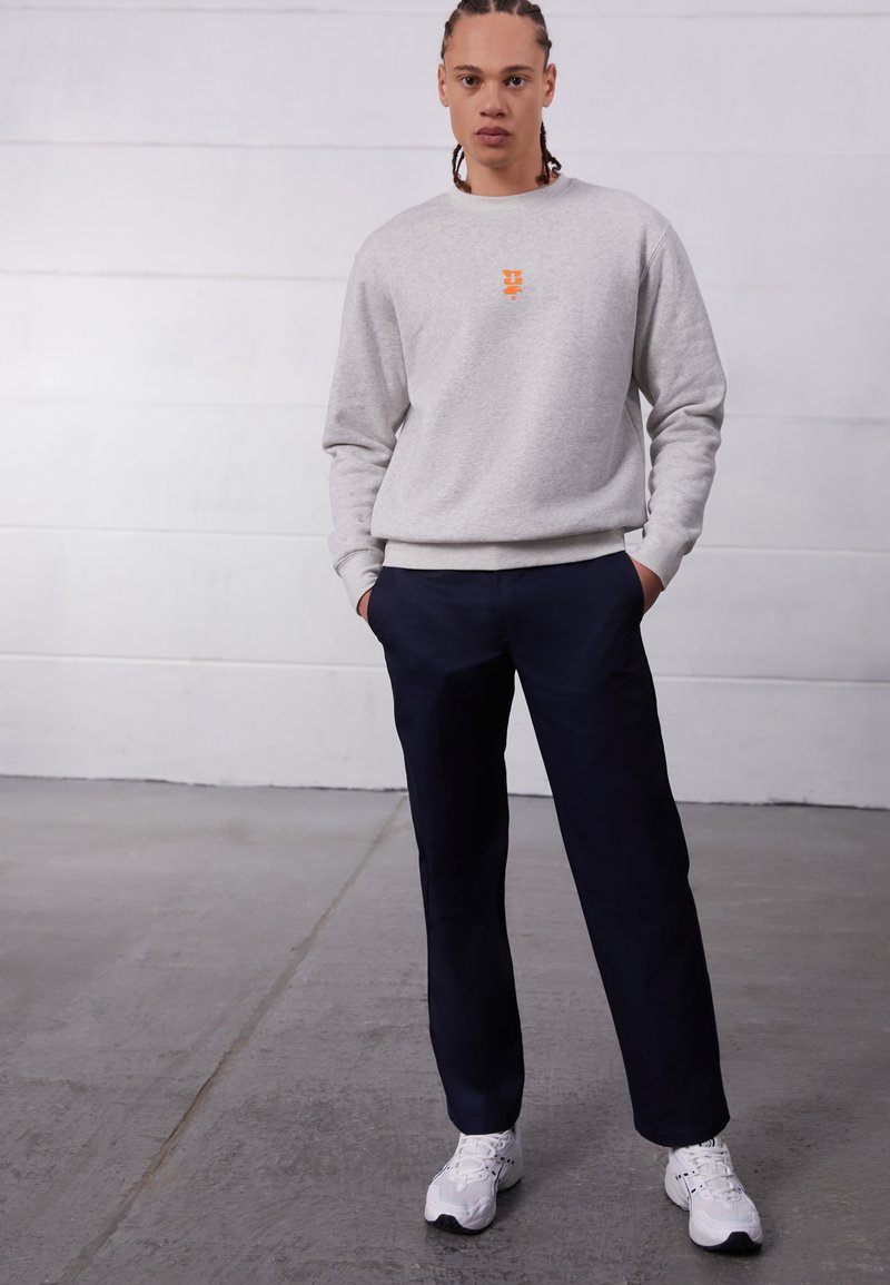 Gray sweatshirt with orange logo, paired with navy pants. The outfit features a relaxed fit and is complemented by white sneakers.