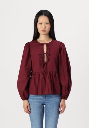 Maroon blouse with puff sleeves, a round neckline, and a keyhole front closure. Made of textured fabric with gathered waist detail.