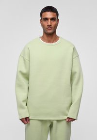 Mintgroene oversized sweatshirt met een gestructureerde afwerking, ronde halslijn en drop schouders, gecombineerd met bijpassende broek in een relaxte pasvorm.